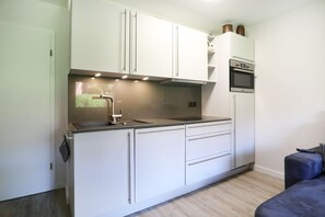 Une cuisine compacte avec des meubles blancs, un évier en acier inoxydable, un four encastré et un petit plan de travail.