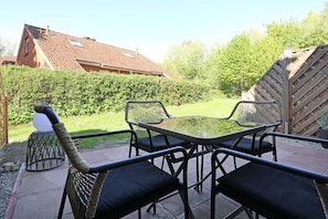 Une terrasse avec une table et des chaises en verre, entourée d’une haie et d’une clôture en bois.