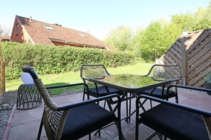A patio with a glass table and chairs, surrounded by a hedge and a wooden fence. - Vacationer village 43c, Germany (Ostseebad Boltenhagen)