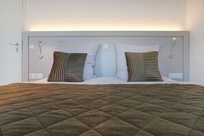 Un lit avec une couverture matelassée, deux oreillers et une tête de lit dotée d’un luminaire.