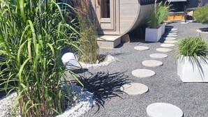 A spa-like structure with a curved roof, surrounded by gravel and stepping stones, and adjacent to a building with a tiled roof. - Apartment sea breeze (Aventoft)
