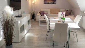 A modern living room with a dining area, white furniture, a flat-screen TV, and a painting on the wall. - Apartment sea breeze (Aventoft)