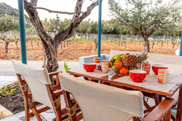 An outdoor dining area with a table set for two, surrounded by chairs, and a view of a vineyard in the background.