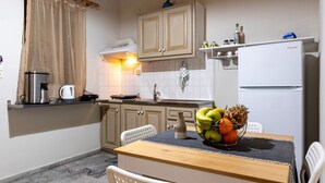 Una cucina funzionale con un tavolo di legno, sedie bianche, un frigorifero e una ciotola di frutta sul ripiano.