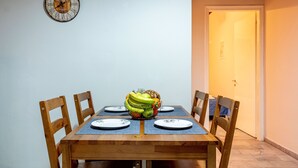 A dining table with four chairs, a fruit bowl, and a wall clock.