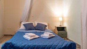 A neatly made bed with a blue quilt, two pillows, and folded towels on the bed.