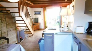 Eine kompakte Küche mit Kühlschrank, Herd und Spüle. Eine Holztreppe führt zu einer weiteren Ebene.