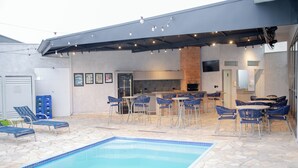 Un área de piscina al aire libre con sillones de descanso, una zona de barbacoa y una cocina.