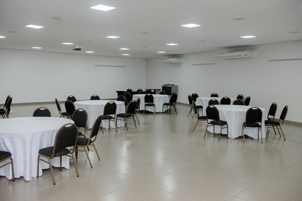 A conference room with multiple tables and chairs, air conditioning units, and a projector on the ceiling. - Colonial Flat Hotel (Itapetininga)