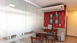 Un pequeño espacio de oficina con un panel de vidrio, una máquina de café y algunas fotos enmarcadas en la pared.
