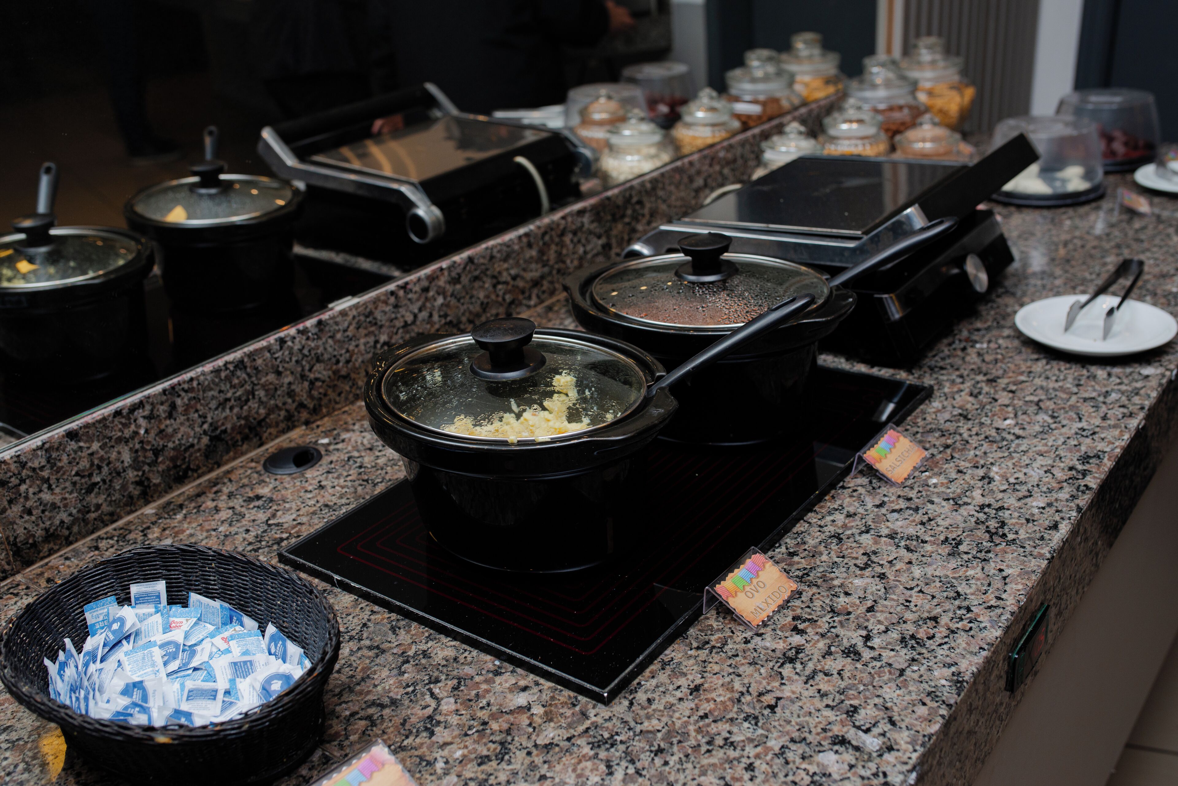 A buffet setup with various food containers and a basket of currency.