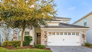 A two-story house with a stone facade, a tiled roof, and a white garage door. - Large Family! Pool & Spa! Epic Champions Gate Resort Near Disney (Davenport)