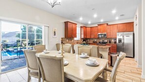 A spacious kitchen with wooden cabinets, a stainless steel refrigerator, and a dining area with a table set for four. - South-Facing Pool & Spa • No Rear Neighbors • Game Room • Near Disney (Davenport)