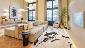 Een moderne woonkamer met een hoekbank, een ronde salontafel en een groot raam met gordijnen.