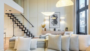 Een moderne woonkamer met een bank, kussens, een salontafel, een trap en een groot raam.