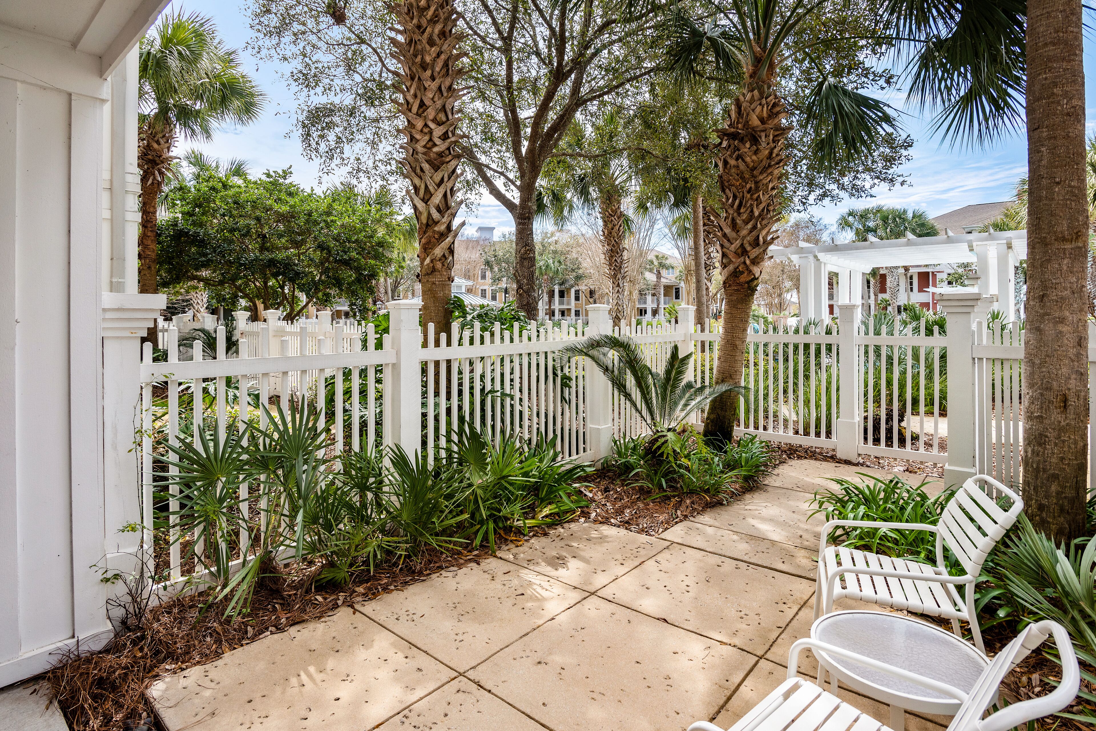 A covered patio area with a white fence, palm trees, and a white bench.