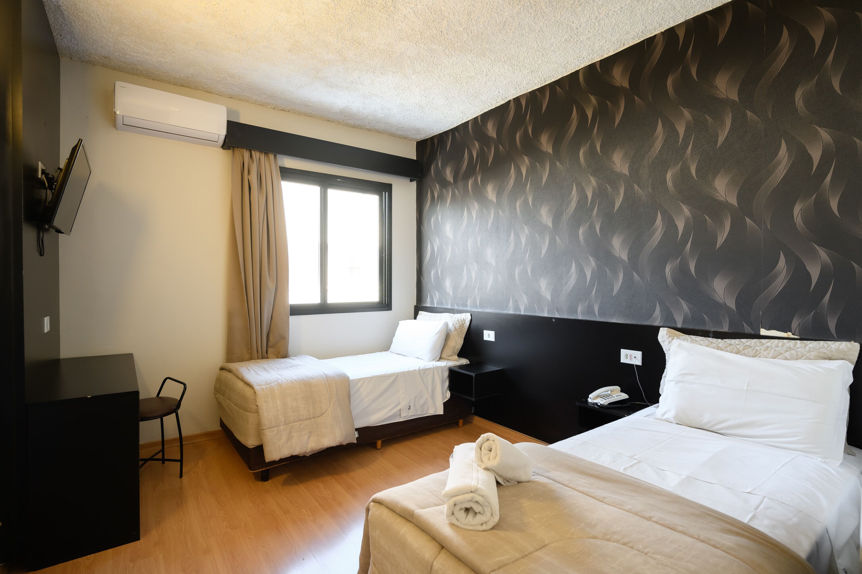 Habitación de hotel con dos camas, un escritorio, una silla y una ventana con cortinas.