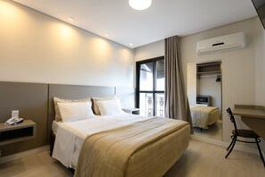 Habitación de hotel con cama, mesita de noche con teléfono, escritorio con silla, armario y aire acondicionado.