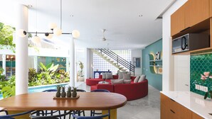 Ein modernes Wohnzimmer mit Essbereich, einem roten Sofa, einer Treppe und einer Küche mit Mikrowelle.