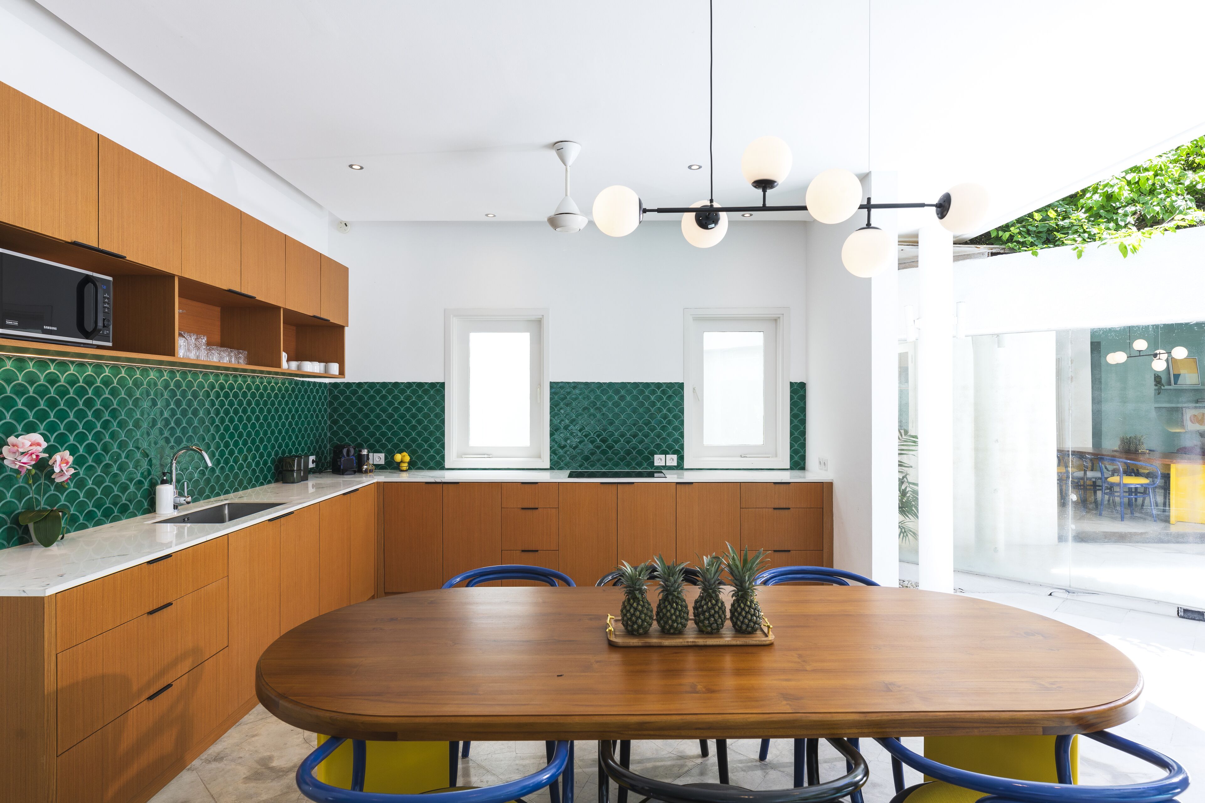 A modern kitchen with wooden cabinets, a green tiled backsplash, and a wooden dining table with chairs.