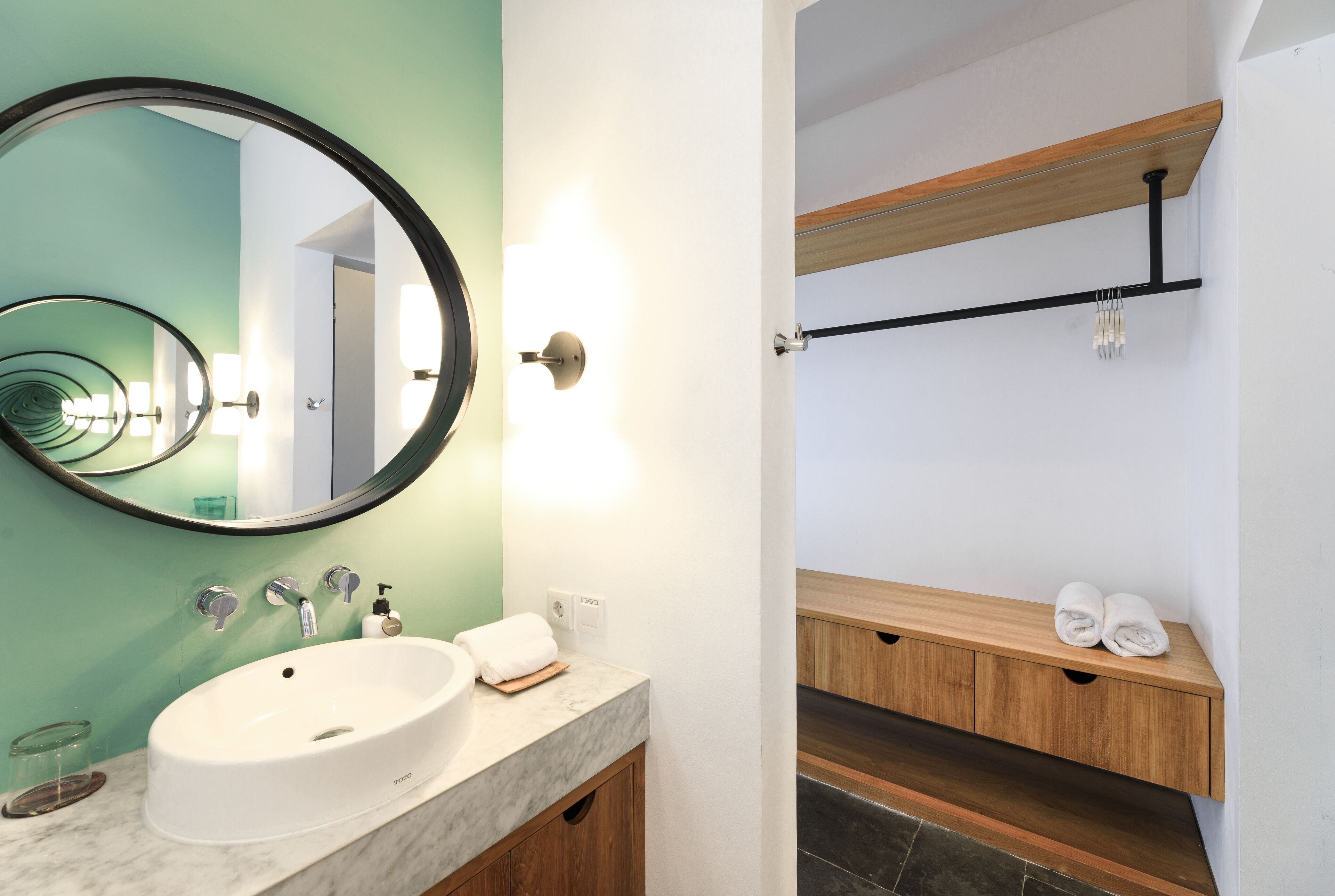 A bathroom with a white sink, a round mirror, and a wooden vanity with a towel rack.