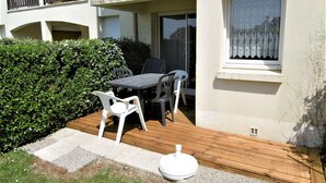 A patio with a table and chairs, a wooden deck, and a hedge.