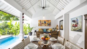 A dining area with a pool view, white walls, and tropical plants. - Villa Atma (Seminyak)