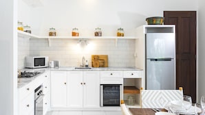 A modern kitchen with white cabinets, a microwave, a refrigerator, and a dining area set with white plates and glasses. - Villa Atma (Seminyak)