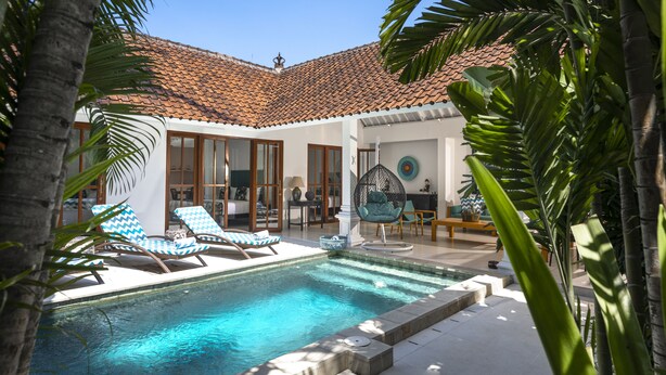 Un espace piscine comprenant des chaises longues, un fauteuil suspendu et un coin repas avec une table et des chaises.