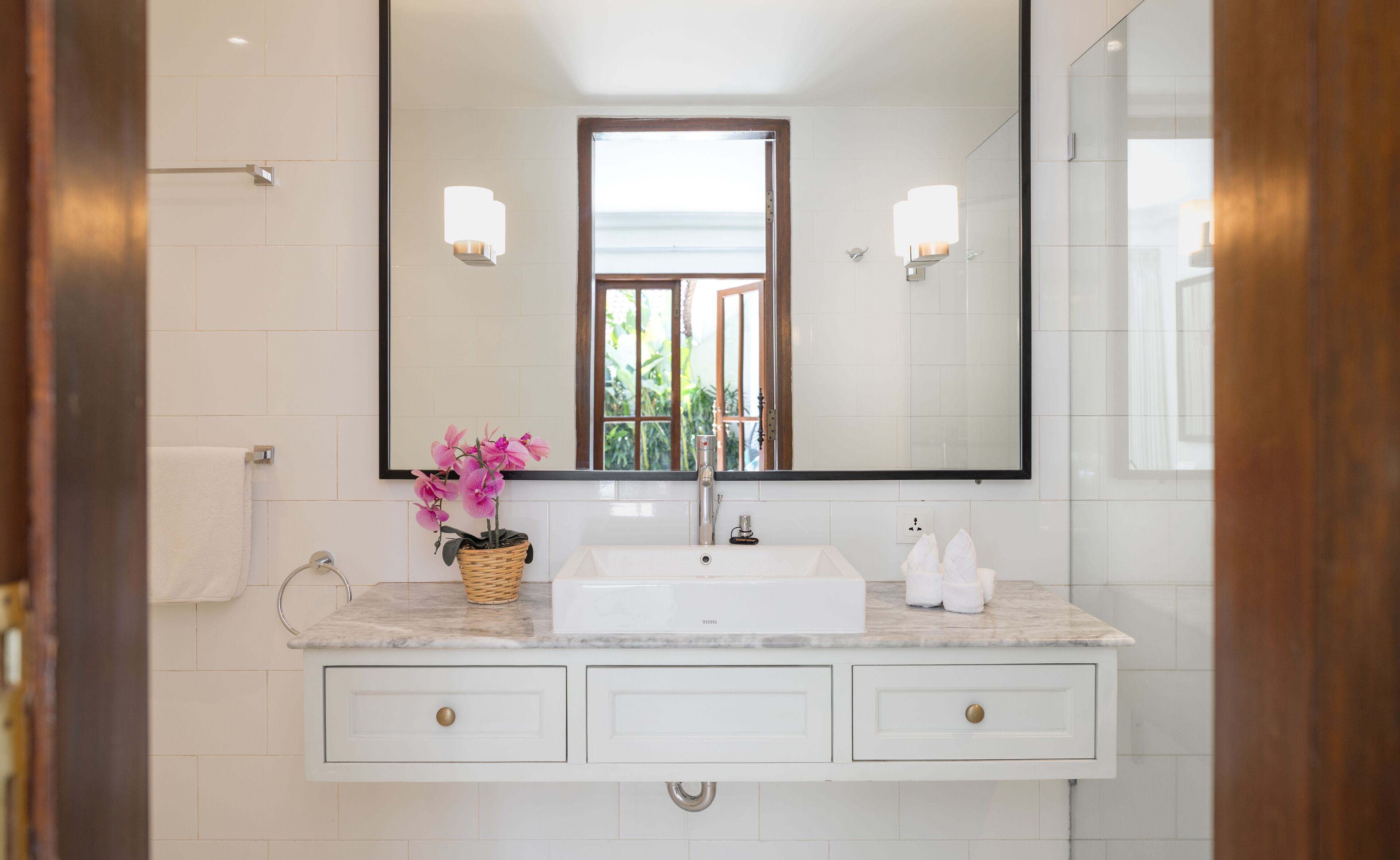 Une salle de bain avec un lavabo blanc, un miroir et une fenêtre.