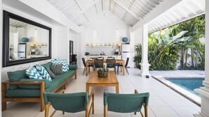 Un salon moderne avec un canapé, des fauteuils, une table à manger et une cuisine en arrière-plan.
