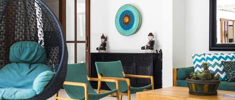 Una sala de estar con un sillón colgante, sillas de madera, una mesa de centro y un sofá con una planta.