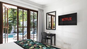 Une chambre avec un lit, un bureau, une chaise, une télévision et une vue sur une piscine et un espace verdoyant.