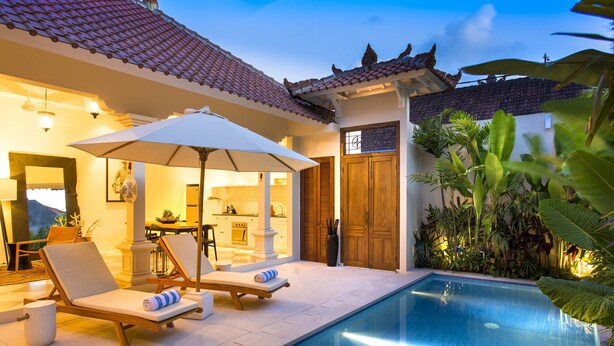 A poolside area with lounge chairs and an umbrella, a kitchen visible through an open door, and a wooden door with a decorative design. - Villa Soleh (Seminyak)