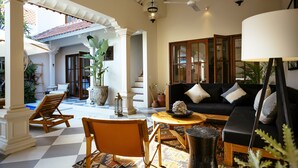 A spacious living area with a checkered floor, a black sofa with cushions, a wooden coffee table, and a large potted plant. - Villa Soleh (Seminyak)