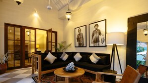 A living room with a black sofa, wooden coffee table, and a patterned rug. There are two framed pictures on the wall, a floor lamp, and a potted plant. - Villa Soleh (Seminyak)