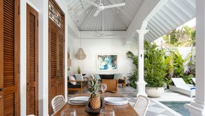 A dining area with a wooden table set for two, white chairs, and a ceiling fan. - Villa Wahah (Seminyak)