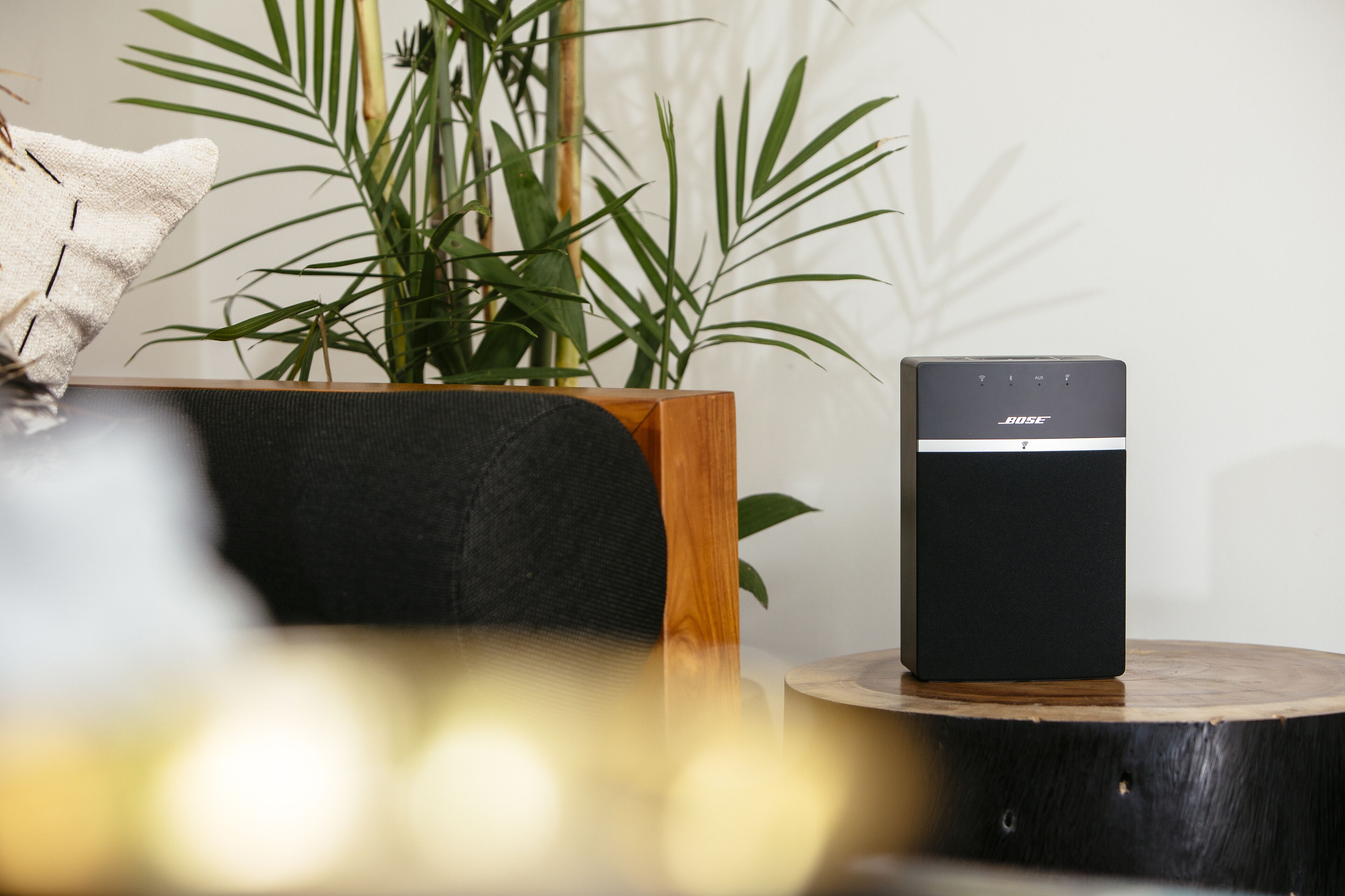 Een zwarte Bose speaker op een houten tafel, met een plant op de achtergrond.