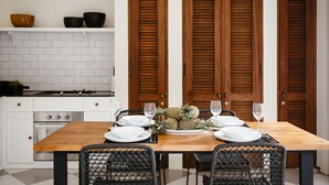 Un comedor con una mesa de madera dispuesta para cuatro personas, rodeada de sillas de mimbre. Se observa un protector contra salpicaduras de baldosas blancas y una estufa blanca al fondo.