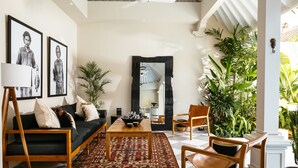 Un salón moderno con sofá, mesa de centro y sillas. Hay una planta grande, un espejo y cuadros en la pared.