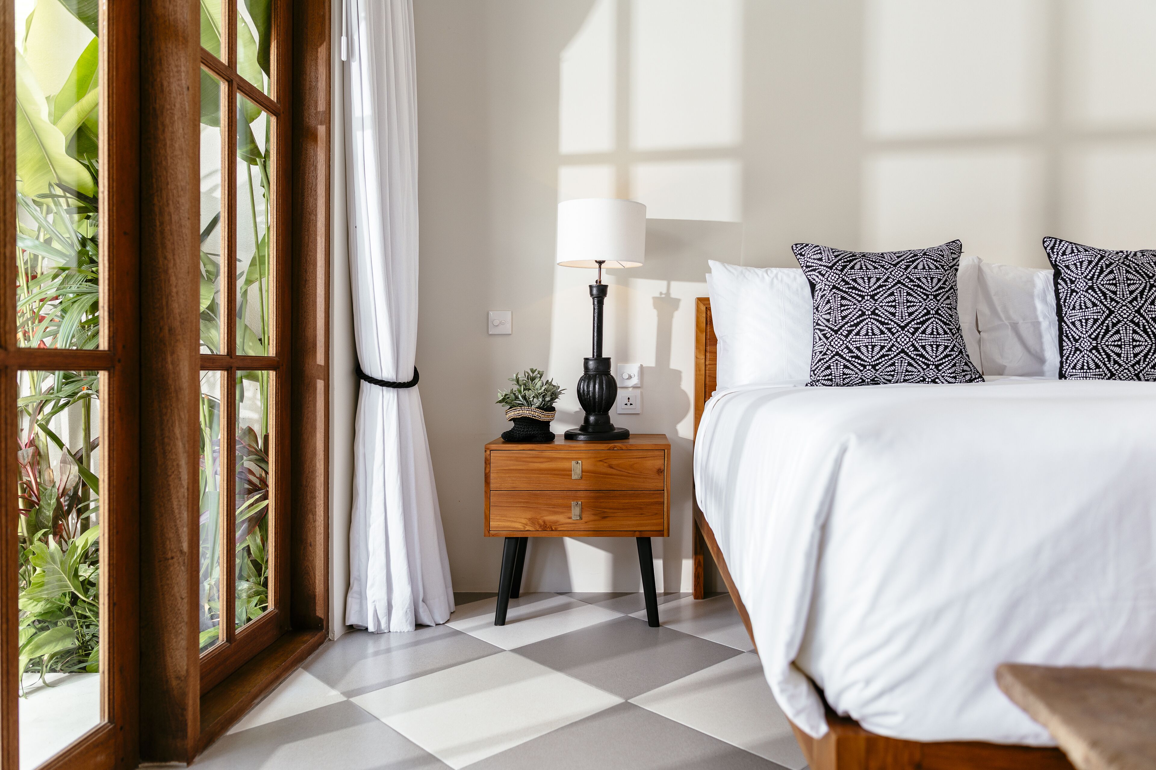 A neatly arranged bedroom with a bed, bedside table, lamp, and curtains.
