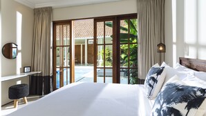 A hotel room with a large bed, a desk, and a view of a pool and outdoor area. - Villa Alliv (Seminyak)