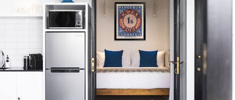 A compact room with a bed, a small table with a potted plant, a microwave, and a refrigerator.