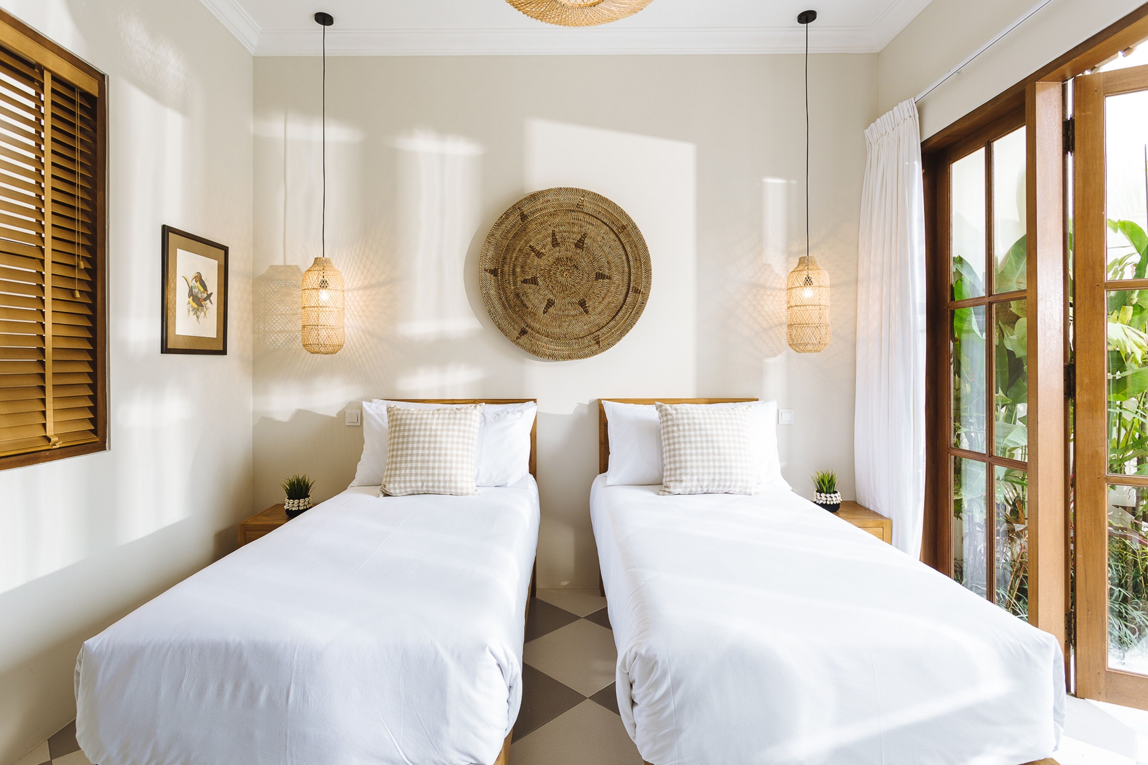 Una habitación con dos camas, un tapiz en la pared y un ventanal con cortinas.