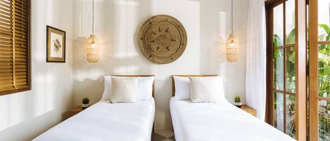 Una habitación con dos camas, un tapiz en la pared y un ventanal con cortinas.