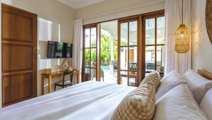 Ein Schlafzimmer mit einem großen Bett, einem Schreibtisch, einem Fernseher und Blick auf einen Außenpool.