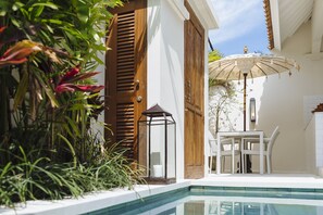 Un espace piscine aménagé avec une table et des chaises, entouré de plantes et doté d’une porte en bois.