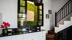 A modern kitchen with a black countertop, white cabinets, and a large window with a green wall behind it. - Pulau Rumah (Seminyak)