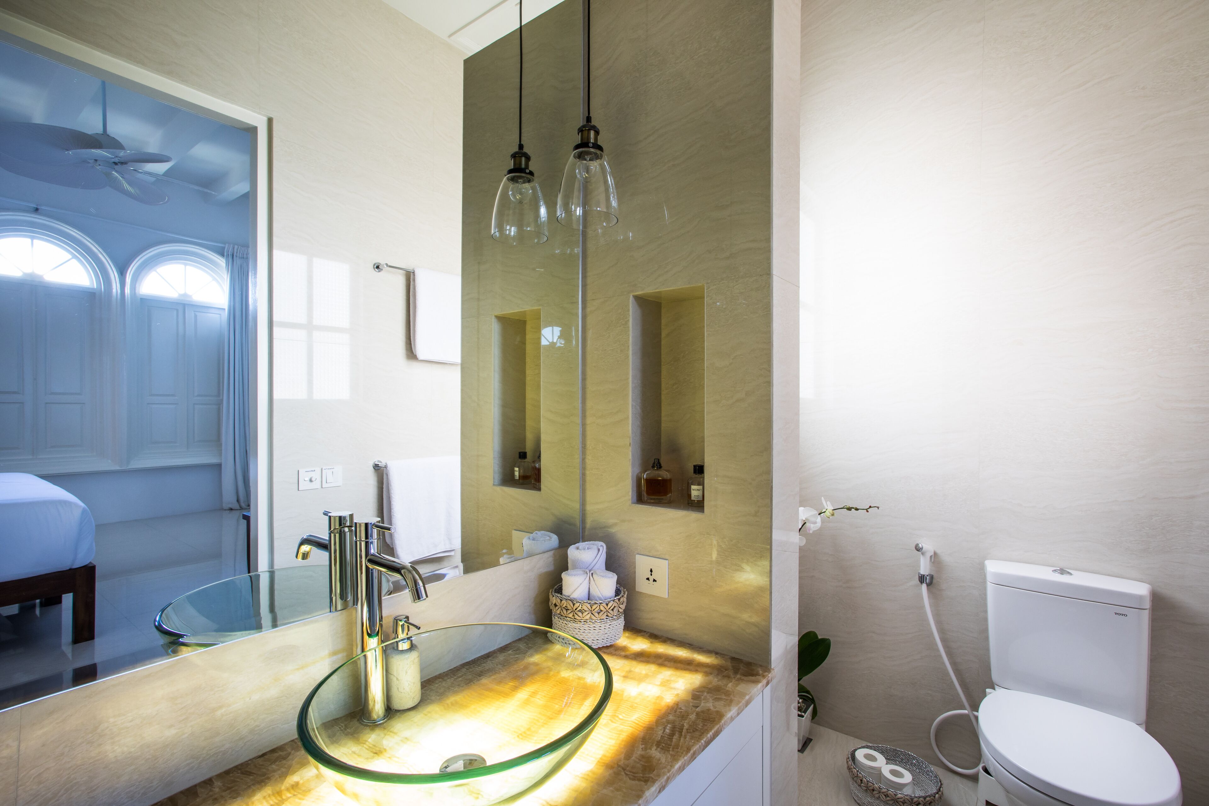 Un baño moderno con un lavabo de vidrio, un espejo grande y un inodoro.