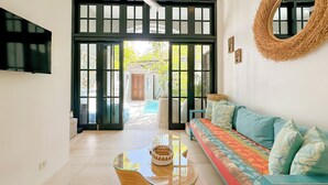 A modern living room with a sofa, a glass coffee table, a television, and a large mirror. - Villa Neno (Seminyak)
